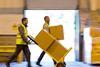 Workers in a warehouse transporting cardboard boxes on a parcel trolley