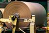 A very large roll of brown paper on machinery at a paper mill.