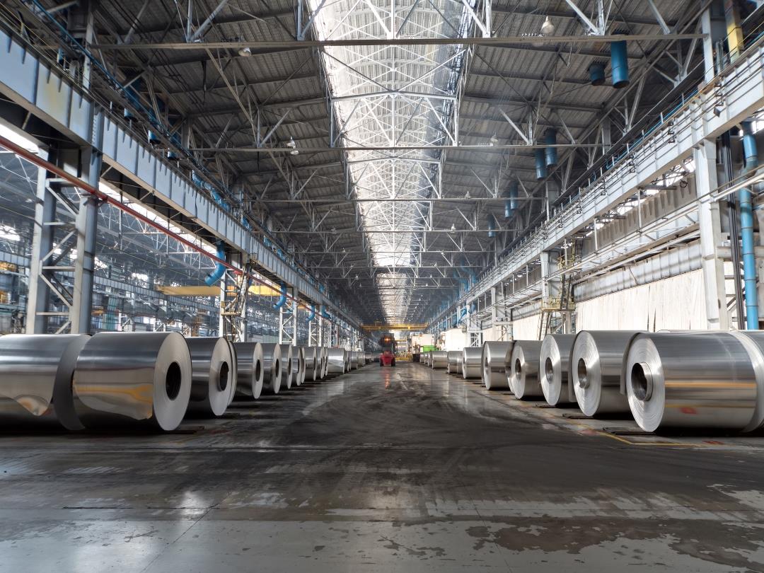 An interior shot of the production shop at an aluminium plant. Rolls of aluminium are placed in rows extending away from…