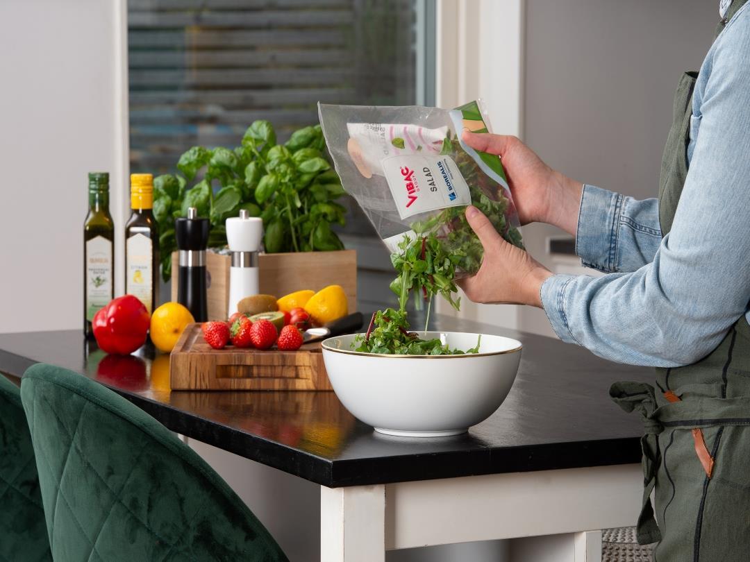A person is pouring a bag of salad into a bowl. The bag is made of a transparent BOPP, labelled 'SALAD' with the Vibac and…