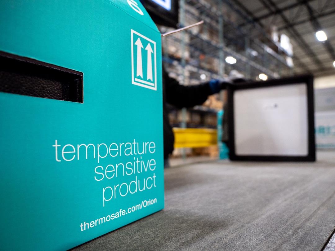 A blue cardboard box sits in the foreground. It reads, 'temperature sensitive product, thermosafe.com/Orion'. A worker and…