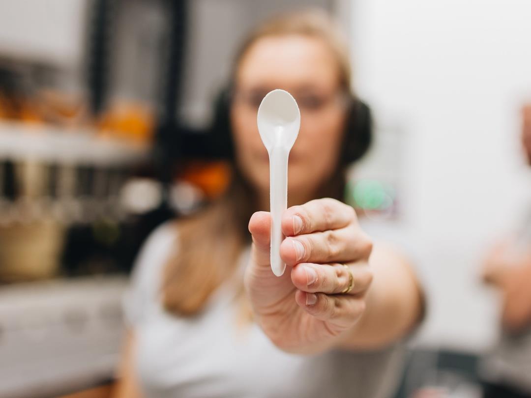 A woman holds a small spoon made of PulPac Dry Molded Fiber up to the camera.