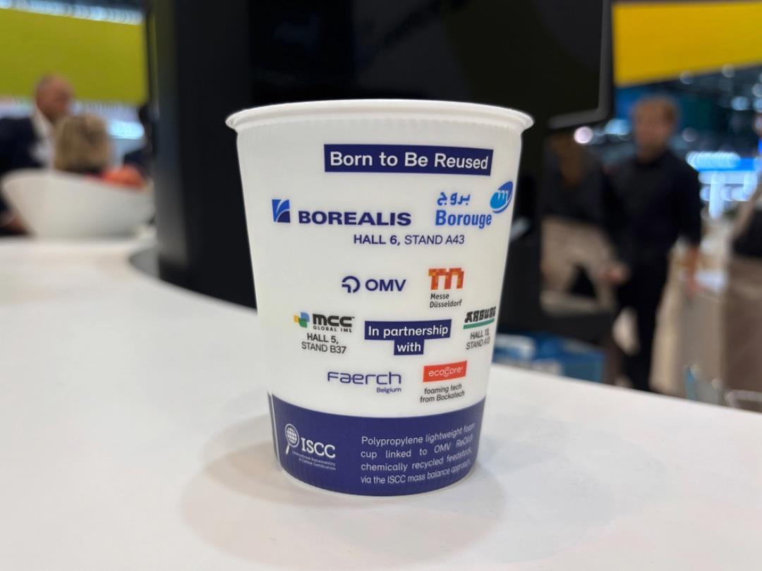 A picture of a reusable cup on a table, the cup has logos of the participating companies on it.
