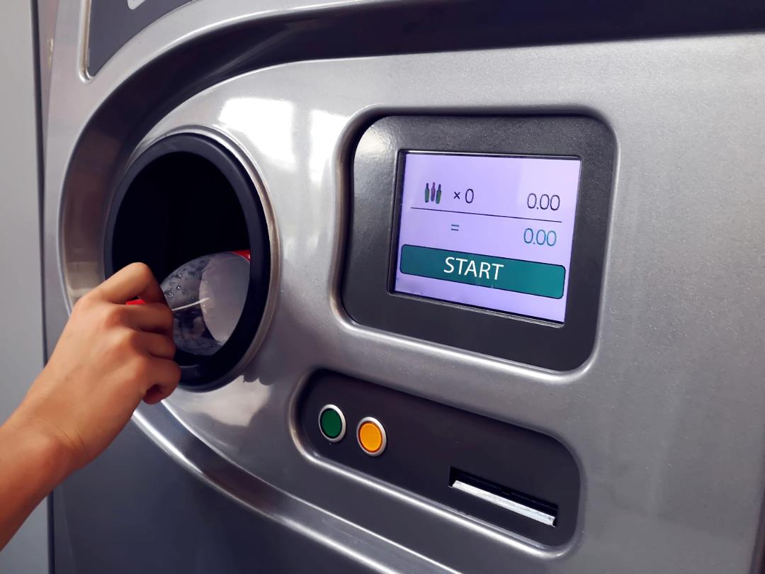 A person inserting an empty bottle into a reverse vending machine.