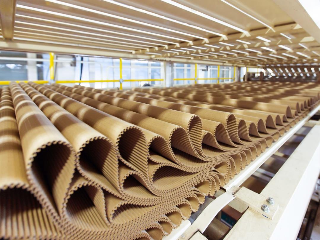 A row of pleat corrugated cardboard lays on a wooden pallet at a factory.
