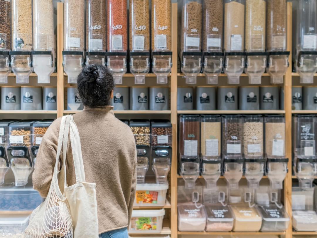 A woman standing in front of a line of refillable packaging dispensers full of dry produce.