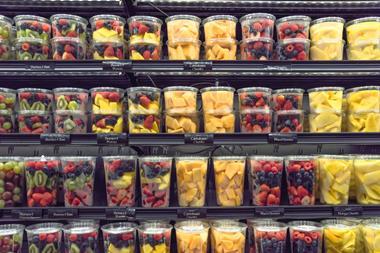 Four supermarket shelves are lined with plastic tubs full of chopped fruits. From left to right, each shelf displays the same assortment of fruit salads; berries and kiwi, berries and pineapple, cantaloupe chunks, mixed berries, and mango chunks.