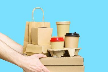 Against a blue background, a pair of hands emerge from the left-hand side of the image. They are holding a pile of unlabelled, undecorated paper packaging. This includes two pizza boxes, cup holders containing coffee cups, clamshell boxes and a paper bag.