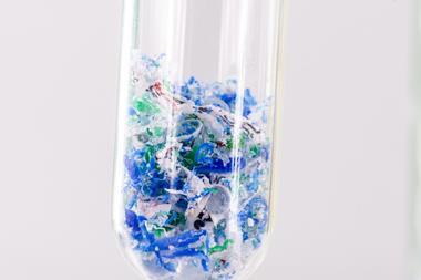 A close-up on the bottom of a test tube. Inside it are tiny flakes of plastic.