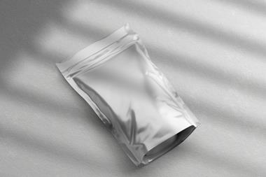 A 3D render of a flexible pouch. It appears to be made of a shiny silver foil, and is laying on a rough white surface. Sunlight appears to be shining through a pair of shutters, casting rectangles of light over the image.