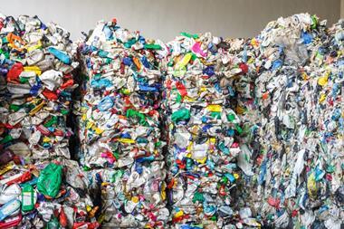 Four large bales of recycled plastic packaging. Various bags, bottles, and tubs have been crushed and tied together at a processing plant.