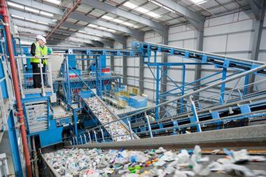A businessman and a worker at a recycling plant stand above a conveyer belt carrying recycled plastic bottles through the waste stream.