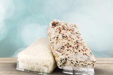 Two packs of white and mixed rice wrapped in flexible plastic packaging sit on a wooden surface.