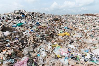 A large pile of landfill towers above the camera, containing waste such as plastic bags, crushed bottles, food packaging, and bin liners.