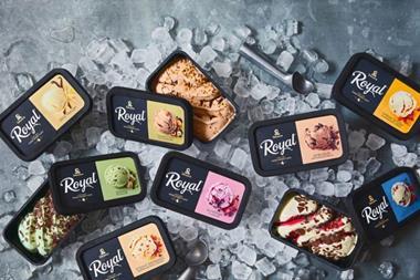A large pile of ice cubes has been arranged on a metal surface. On top of it are two ice cream scoopers in amongst various black ice cream tubs with Diplom-IS Royal branding. Some of the boxes have been opened to reveal the ice cream inside.