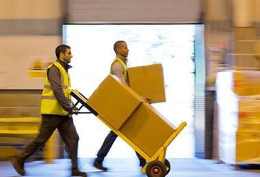 Workers in a warehouse transporting cardboard boxes on a parcel trolley