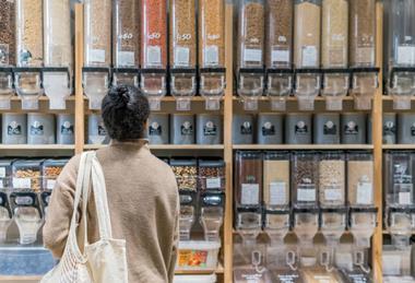 A woman standing in front of a line of refillable packaging dispensers full of dry produce.