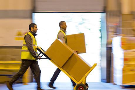 Workers in a warehouse transporting cardboard boxes on a parcel trolley