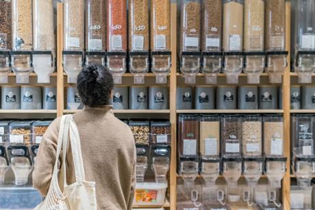 A woman standing in front of a line of refillable packaging dispensers full of dry produce.