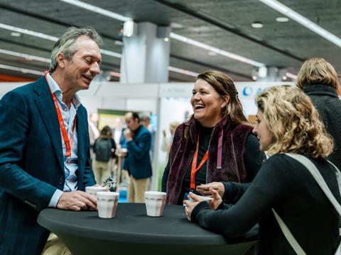 Three Sustainable Packaging Summit delegates talking around a table - two are stood up and one is sat down