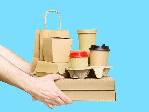 Against a blue background, a pair of hands emerge from the left-hand side of the image. They are holding a pile of unlabelled, undecorated paper packaging. This includes two pizza boxes, cup holders containing coffee cups, clamshell boxes and a paper bag.