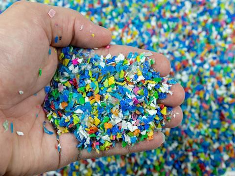 A pile of colourful polymer pellets viewed from above. A hand has scooped up some of the flakes and is holding them up towards the camera.