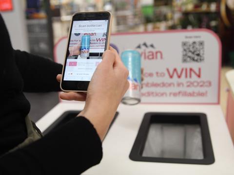 Two hands are visible to the camera. The left is holding an evian can at arm’s length; the other is holding a smartphone and using it to scan a barcode on the can. The can is being held over an evian-branded recycling bin in a Sainsbury’s supermarket.