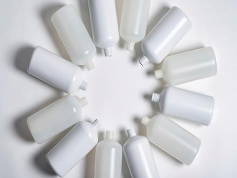 A series of plastic bottles, all without lids, have been sorted into a circular formation with their necks facing inwards. They are laying against a white surface.