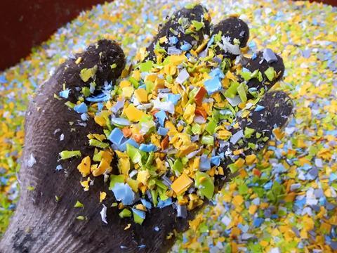 A gloved hand scoops a handful of plastic flakes from a pile.