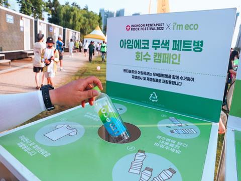 A hand extends from off-camera, holding a bottle labelled 'I'm Eco'. It is being held over a recycling bin, on which is written 'Incheon Pentaport Rock Festival 2022 x I'm Eco'.