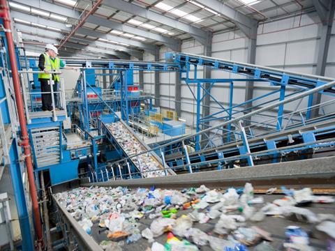 A businessman and a worker at a recycling plant stand above a conveyer belt carrying recycled plastic bottles through the waste stream.