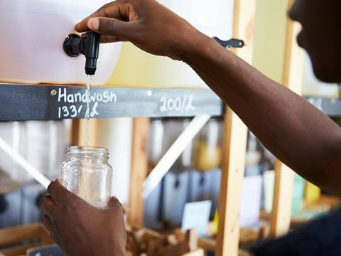 A man is holding a jar beneath a nozzle labelled 'handwash'. He is pumping the liquid into the jar.