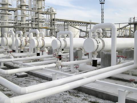 Heat exchangers at an oil refinery. The tanks are long, narrow, white cylinders, with pipes coming from them in geometric patterns. There are red valves at various points on the machinery.