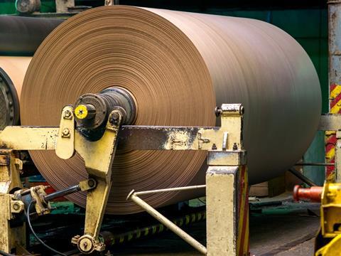 A very large roll of brown paper on machinery at a paper mill.