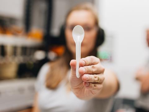 A woman holds a small spoon made of PulPac Dry Molded Fiber up to the camera.