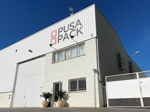 An exterior shot of Pusa Pack's liner bag plant. It is a white building with grates on the windows and the Pusa Pack logo painted onto its front face.