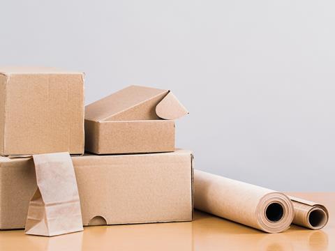 A pile of cardboard boxes, a paper bag, and rolls of paper wrapping are all displayed on a wooden surface.